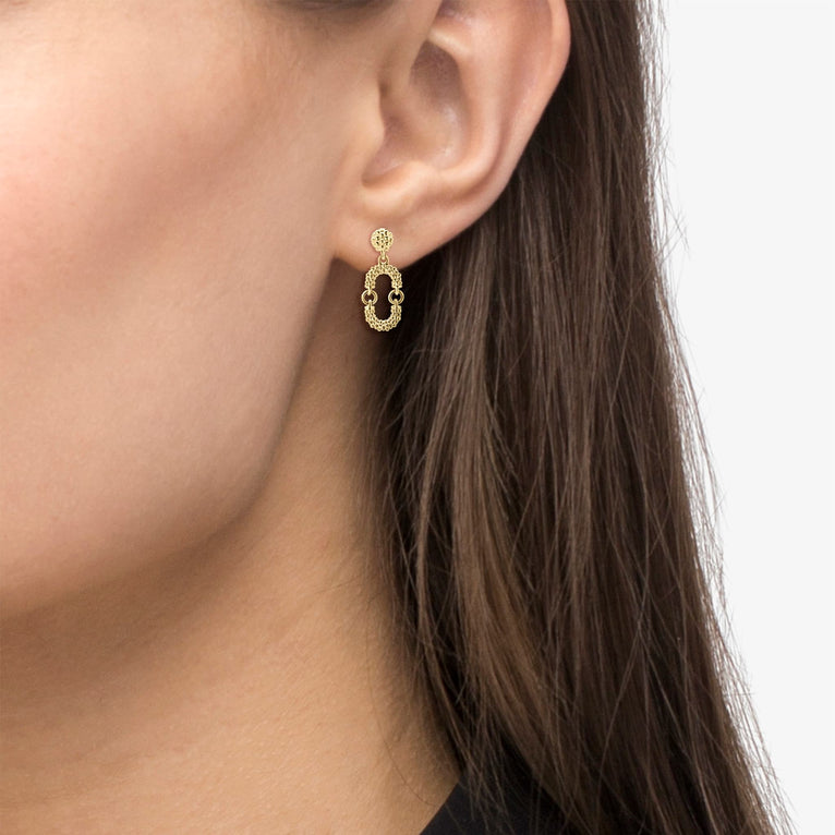 A close-up of a woman wearing a pair of drop earrings with a link motif of 18K gold with superfine Caviar beads. 