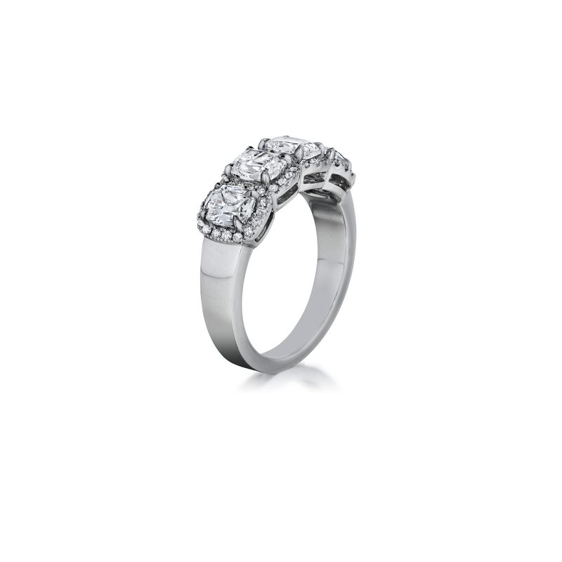 A white gold ring is angled to the right in the middle of a white background. The ring features four radiant-cut diamonds surrounded by round-shaped diamond halos.
