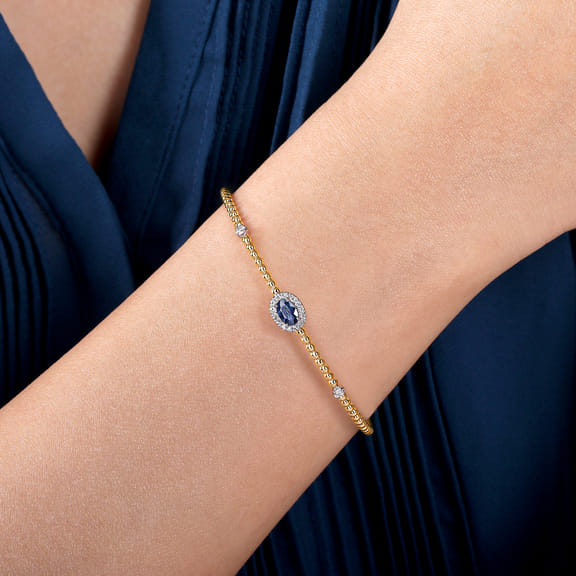 Model wearing the Gabriel & Co Bujukan bangle, showing the blue sapphire and diamond halo centered on the wrist.