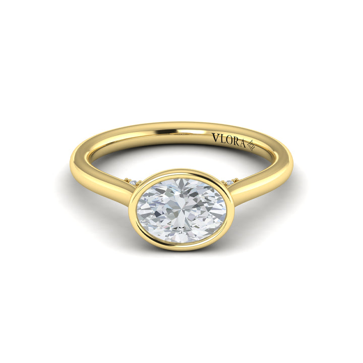 A front view of a yellow gold engagement ring is set against a white background. The engagement ring features a bezel-set east-west oval diamond center stone, cradled in a cathedral arch, and has subtle pavé detailing around the yellow gold band.