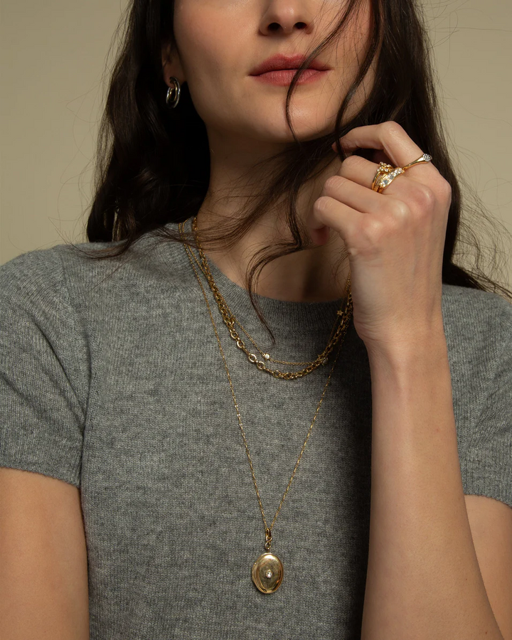 Model wearing the Infinity diamond and gold locket on a long gold chain over a gray shirt