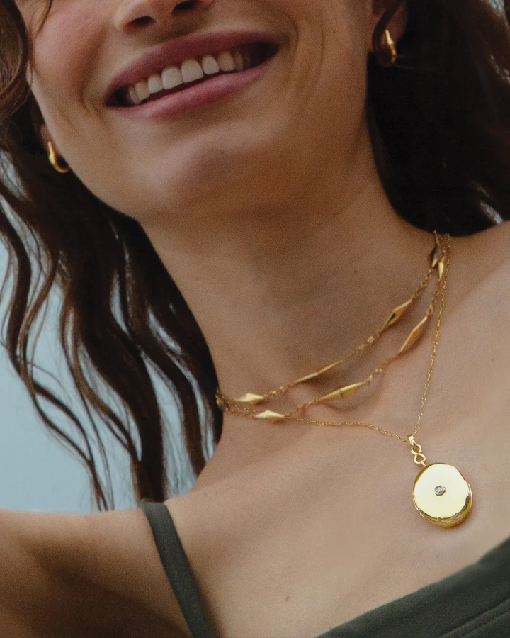 Model wearing the Infinity diamond and gold locket necklace layered with shorter gold necklaces
