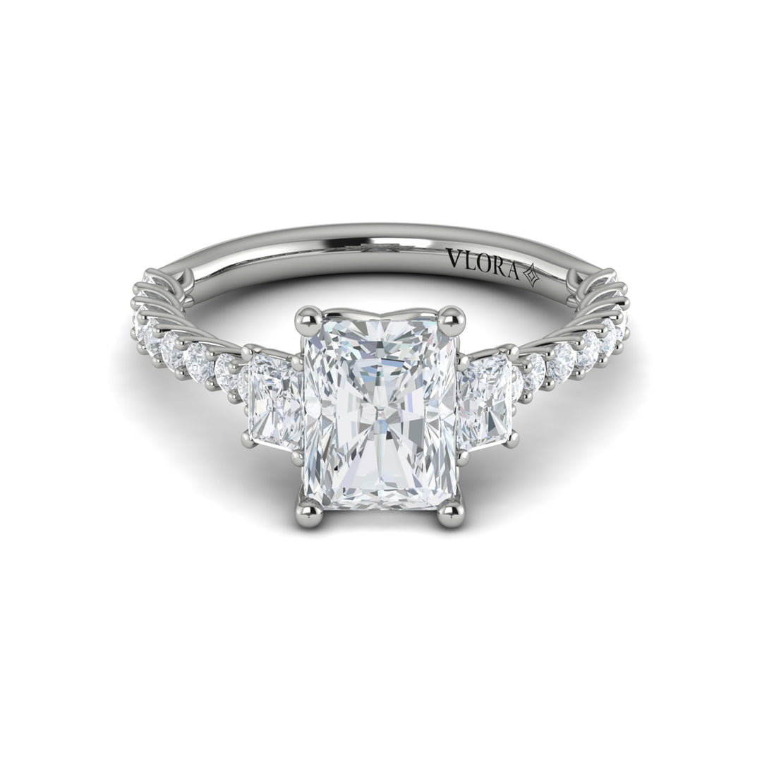 A front view of a white gold engagement ring is set against a white background. The engagement ring features a center emerald cut diamond flanked by two emerald cut side diamonds, an intricate woven setting, and a diamond-set band.