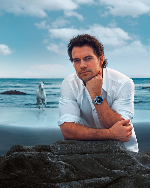 Man in a white shirt wearing the LONGINES HydroConquest L3.788.4.90.6 while leaning on coastal rocks beside the ocean.
