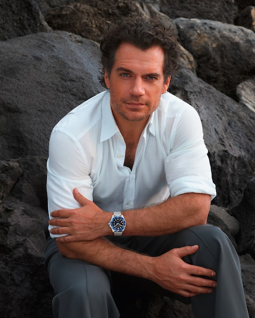 Man seated among rocks wearing the LONGINES HydroConquest L3.788.4.90.6 with a white shirt and dark trousers.