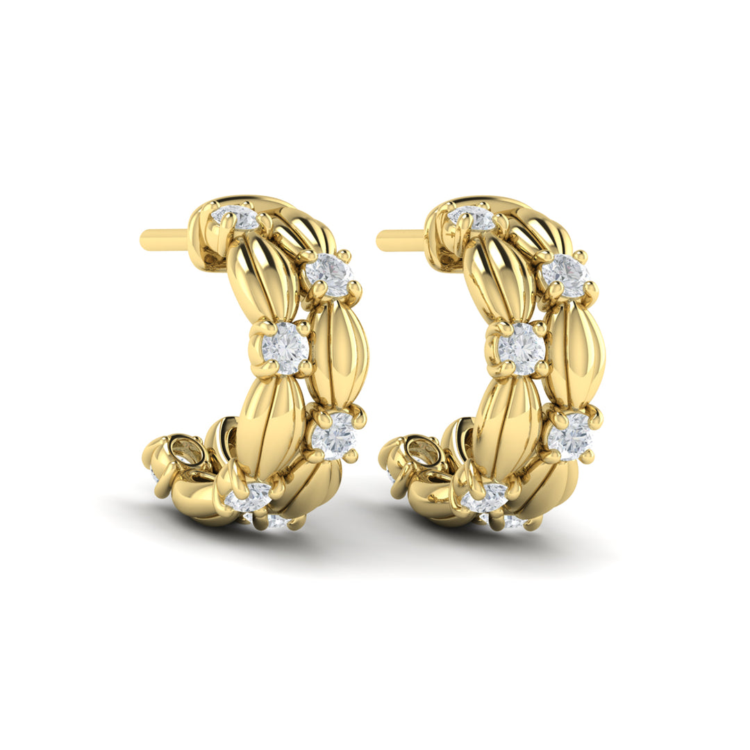 An angled view of yellow gold hoop earrings set against a white background. The sculptural hoop earrings feature two rows of brilliant diamonds and delicate scallop shells.