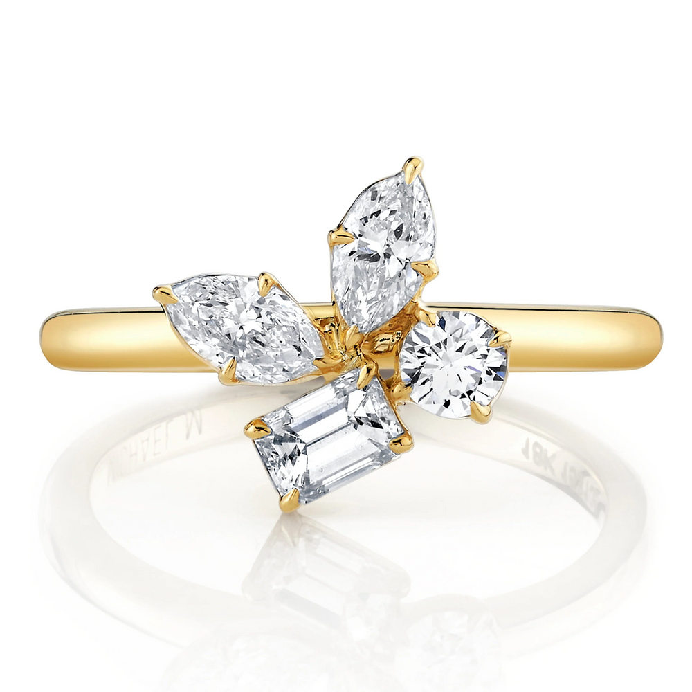A close-up view of a yellow gold ring against a white background. The ring features marquise, pear, and emerald cut stones in a cluster design center piece on a yellow gold band.