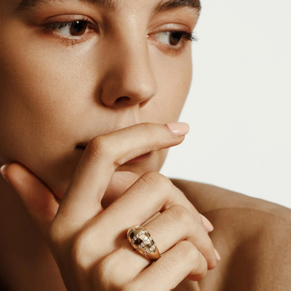 A close-up of a woman holding her hand up to her mouth showcasing the yellow gold ring on her wedding finger. The ring features diamond-set striped row stations and a yellow-gold band.