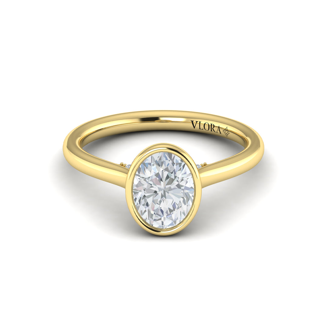 A front view of a yellow gold engagement ring is set against a white background. The engagement ring features a bezel-set oval diamond center stone with a cathedral setting, and has subtle pavé detailing around the yellow gold band.