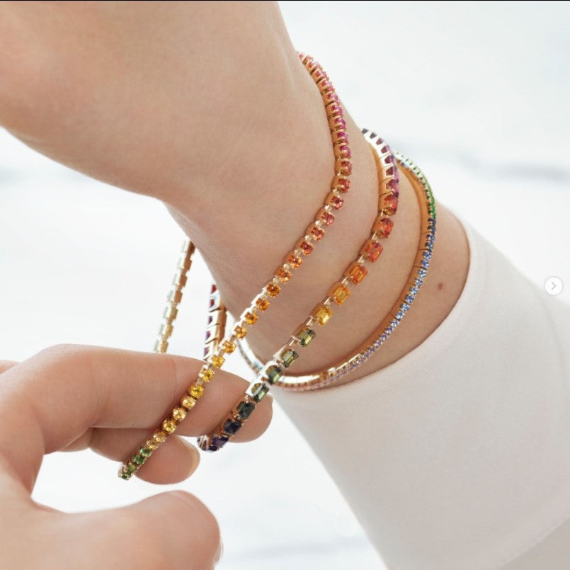 Close-up of a wrist wearing colorful gemstone tennis bracelets, with one bracelet stretched outward