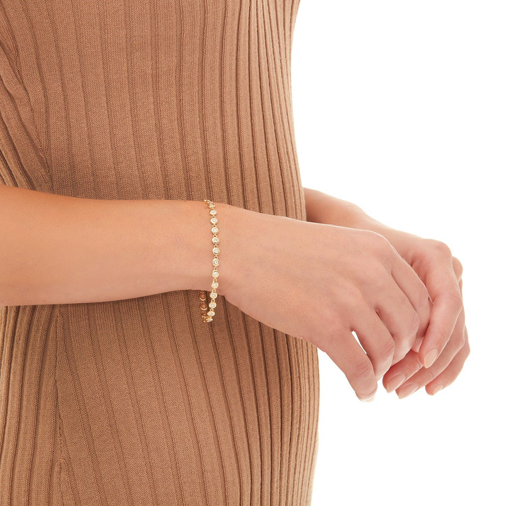 A close-up of a woman wearing a brown striped dress and holding her hands showcasing the bracelet on her wrist. The bracelet features round-shaped diamonds with a halo.