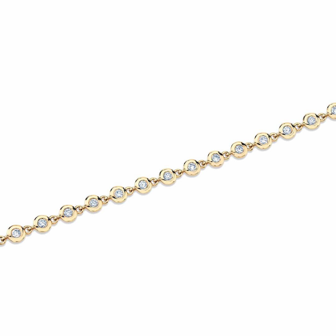 A top view of a yellow gold diamond tennis bracelet laid out across a white background. The diamond bracelet features round bezels with diamonds.