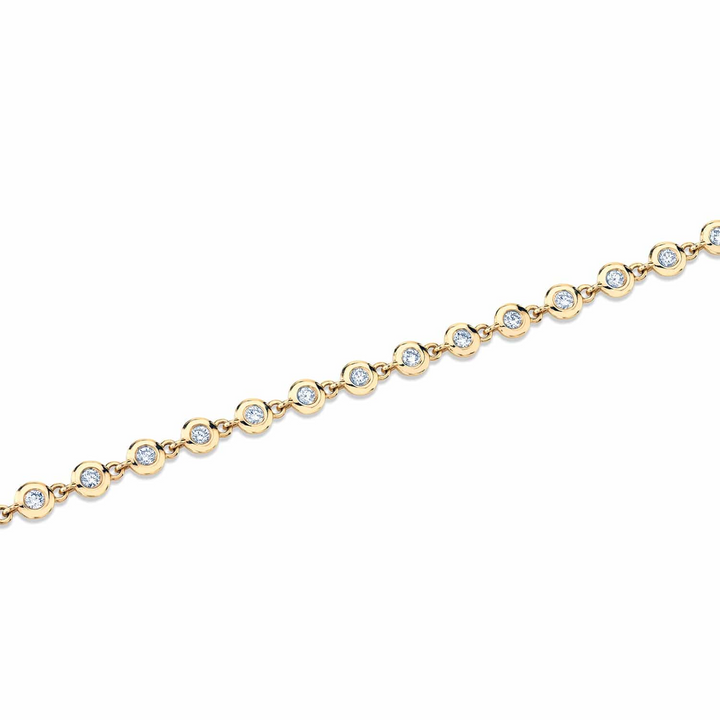 A top view of a yellow gold diamond tennis bracelet laid out across a white background. The diamond bracelet features round bezels with diamonds.