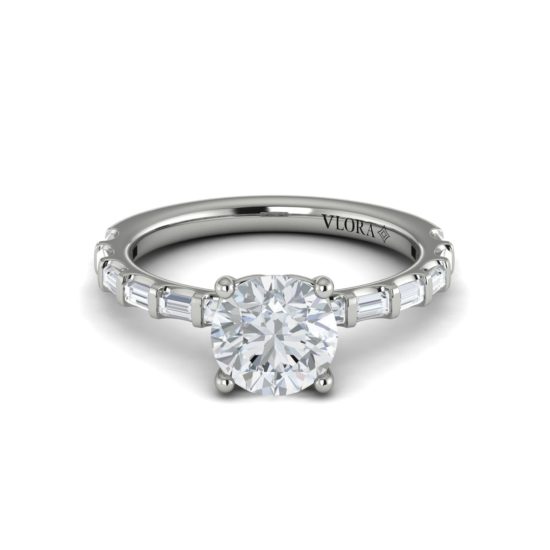A front view of a white gold engagement ring is set against a white background. The engagement ring features a center round cut diamond, an Art Deco design, and a streamlined band of bar-set baguette diamonds.