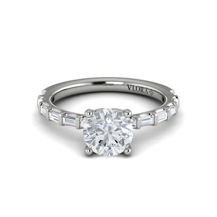 A front view of a white gold engagement ring is set against a white background. The engagement ring features a center round cut diamond, an Art Deco design, and a streamlined band of bar-set baguette diamonds.