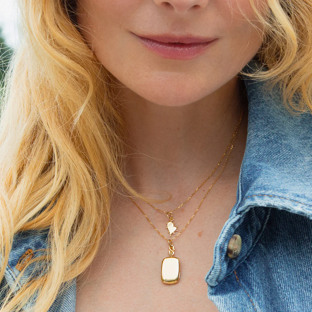 Model wearing the Slim Britt gold locket necklace layered with a smaller heart necklace