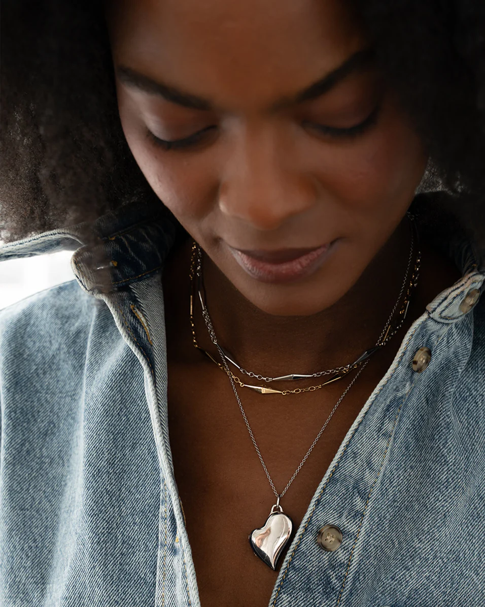 Model wearing the slim sterling silver heart locket necklace, showing the pendant against a white top and denim jacket.