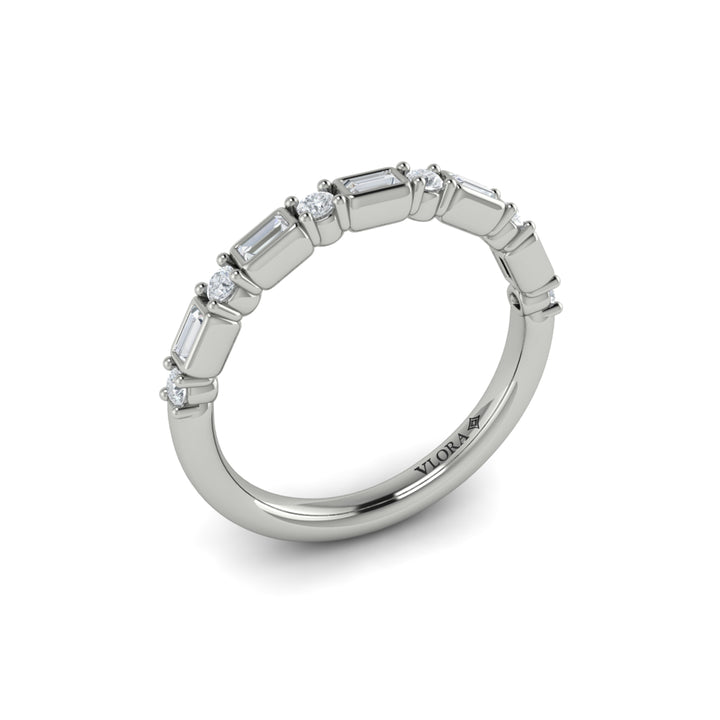 An angled view of a white gold band set against a white background. The ring features a half-eternity east-west emerald and round diamonds alternating design.