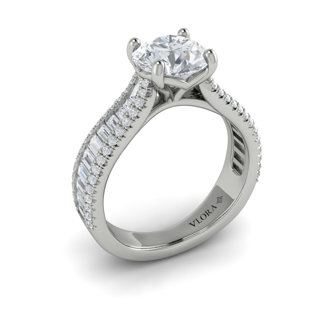 An angled view of a white gold engagement ring is set against a white background. The engagement ring features a round center diamond, Vlora's signature V-shaped setting, a three-dimensional channel set baguette diamond band, and a cathedral design.