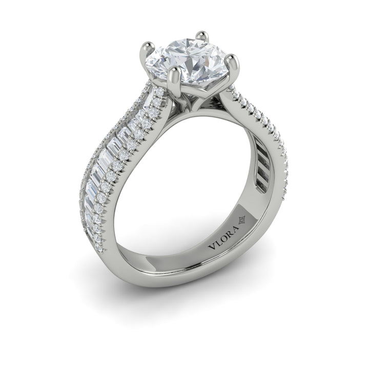 An angled view of a white gold engagement ring is set against a white background. The engagement ring features a round center diamond, Vlora's signature V-shaped setting, a three-dimensional channel set baguette diamond band, and a cathedral design.