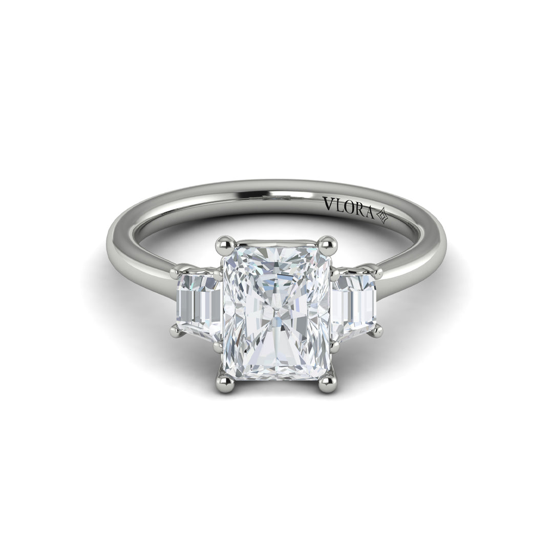 A front view of a white gold engagement ring is set against a white background. The engagement ring features an emerald cut center diamond, flanked by complementary emerald cut side stones, in a woven setting. 