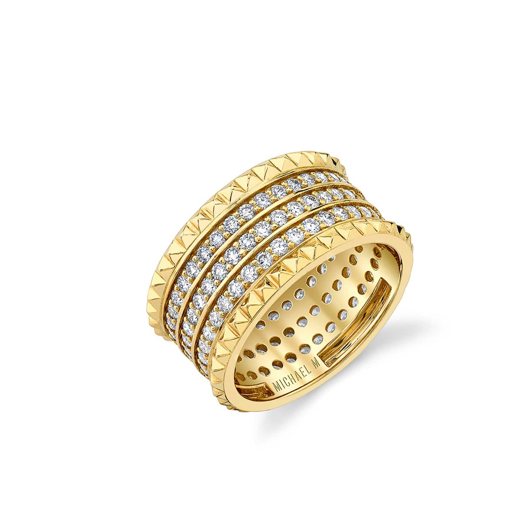 An angled view of a yellow gold diamond ring against a white background. The ring features a gold band ring with three rows of sparkling round diamonds set pavé between two bands of miniature pyramid studs.