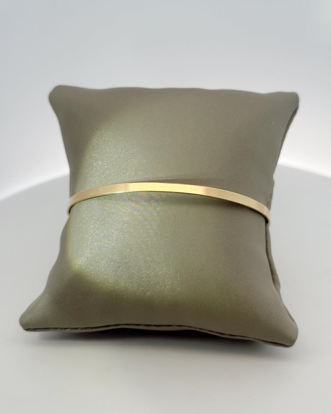 The Essential 14K yellow gold bangle around a gray display pillow, showing its slim polished band