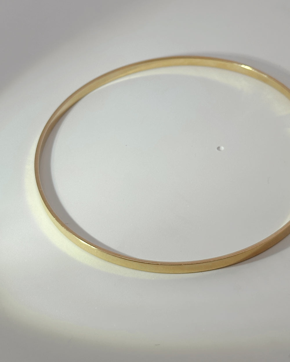 The Essential yellow gold bangle lying flat on a white surface, showing its continuous circular shape