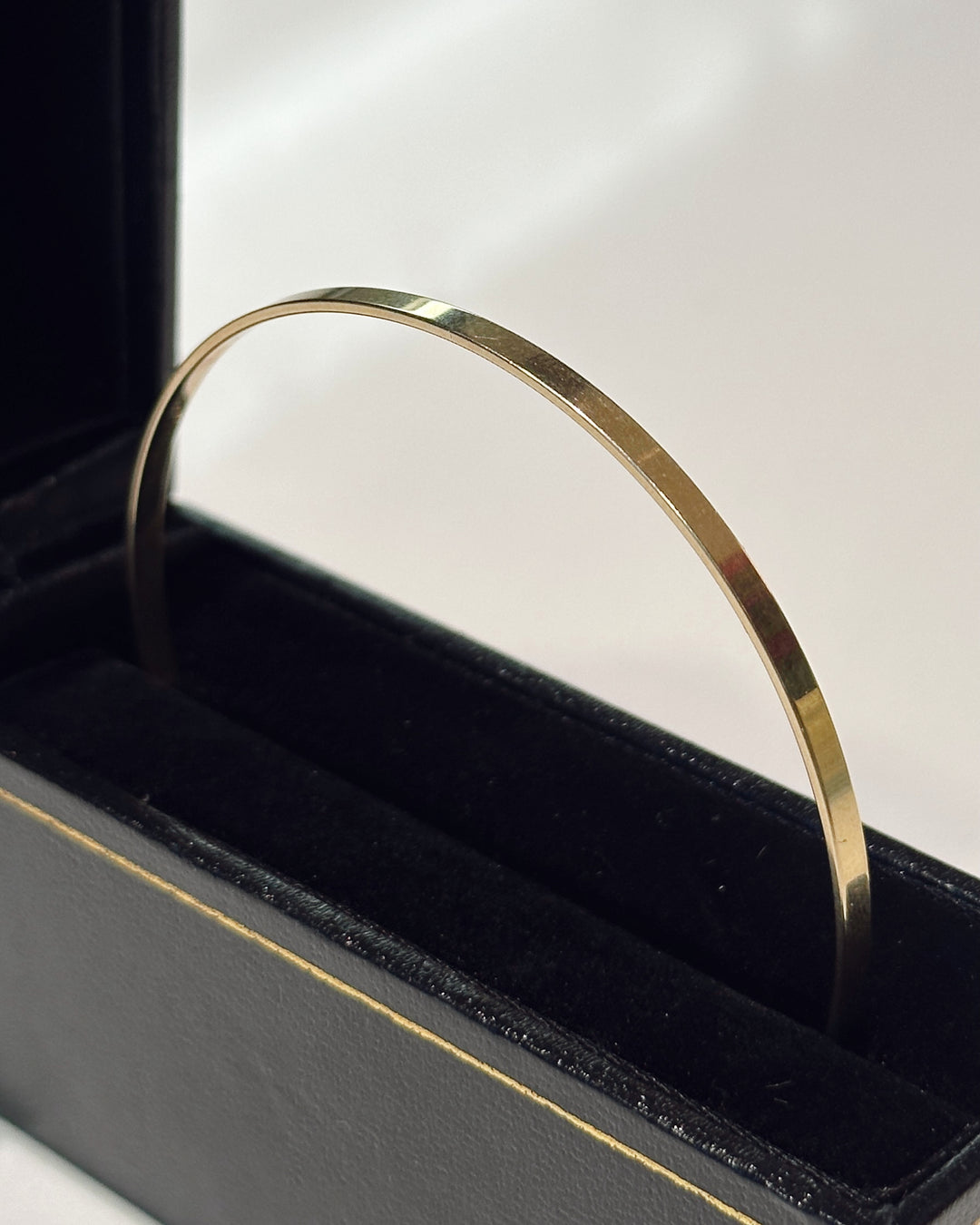 The Essential 14K yellow gold bangle standing upright in an open black jewelry box