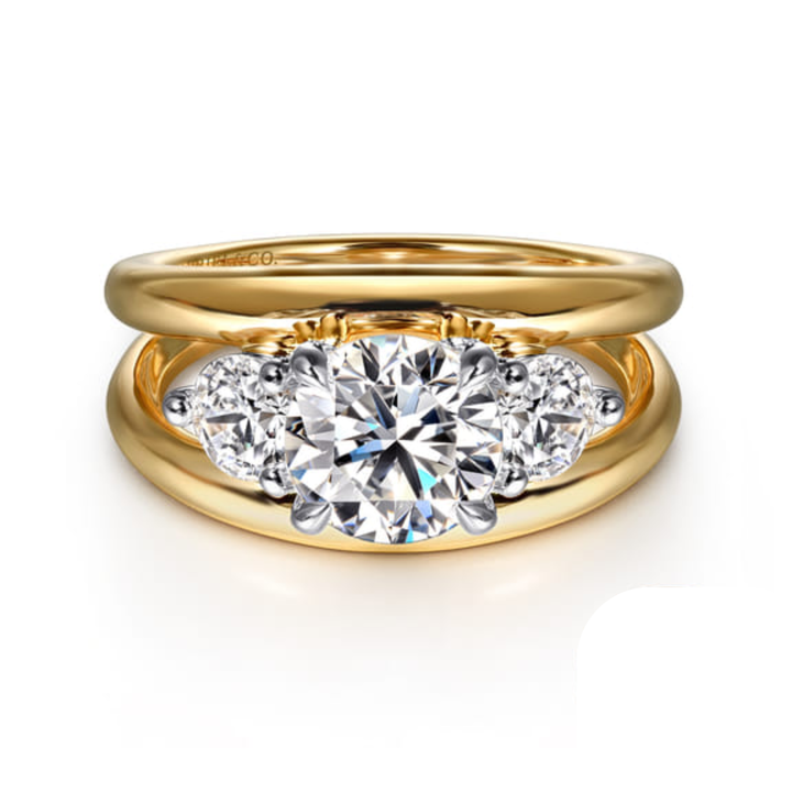 Front view of a three stone round diamond engagement ring with white gold prongs and a wide yellow gold split shank band.