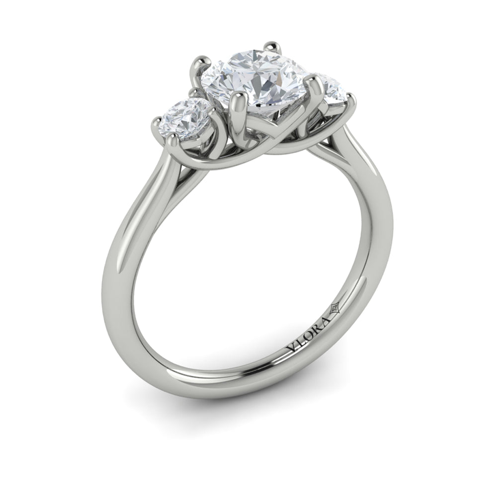 An angled view of a white gold engagement ring is set against a white background. The engagement ring features a round center diamond flanked by two smaller round diamonds, set in an interlaced design.