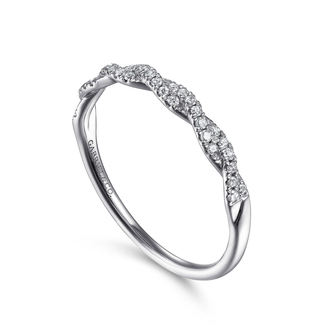 A white gold ring is angled to the right in the middle of a white background. The ring features a diamond-set twist design and Gabriel & Co engraved inside the ring on the left side.