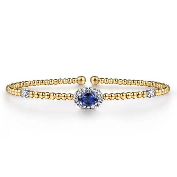 Gabriel & Co Bujukan bangle with an oval blue sapphire, white gold diamond halo and beaded yellow gold band.