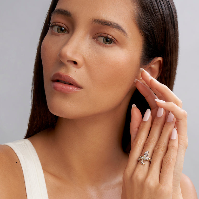 A close-up of a woman holding her hand up to her cheek, showcasing the ring on her middle finger. The ring features a snake motif with Sterling silver Caviar beading highlighted by 18K gold stations.
