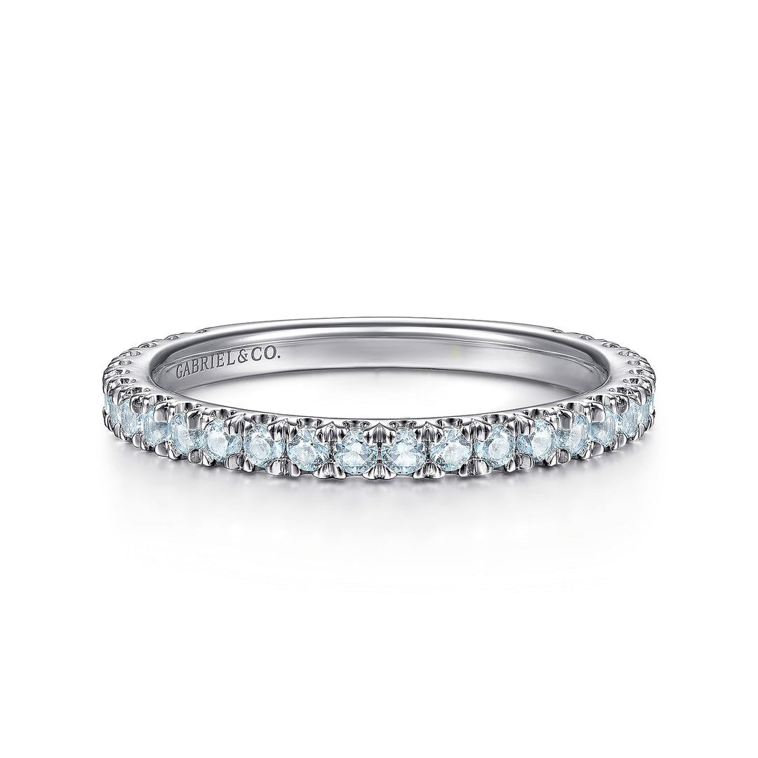 A front view of a white gold wedding band against a white background. The ring features sky blue topaz gemstones set in place by small prongs in gleaming white gold.