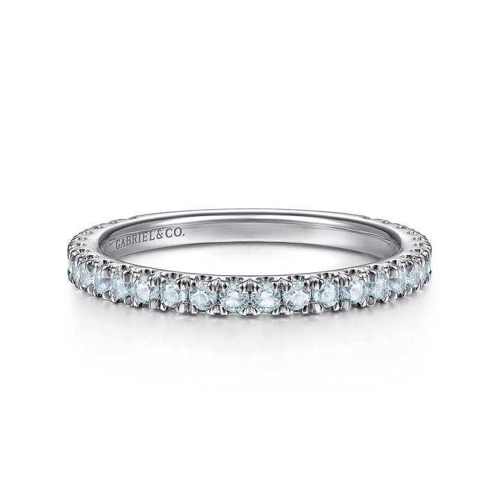 A front view of a white gold wedding band against a white background. The ring features sky blue topaz gemstones set in place by small prongs in gleaming white gold.