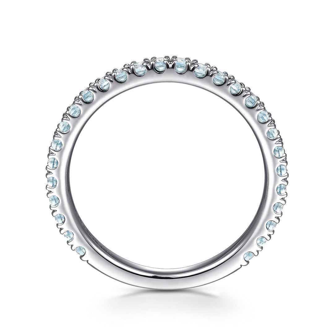 A side profile view of a white gold wedding band against a white background. The ring features sky blue topaz gemstones set in place by small prongs in gleaming white gold.