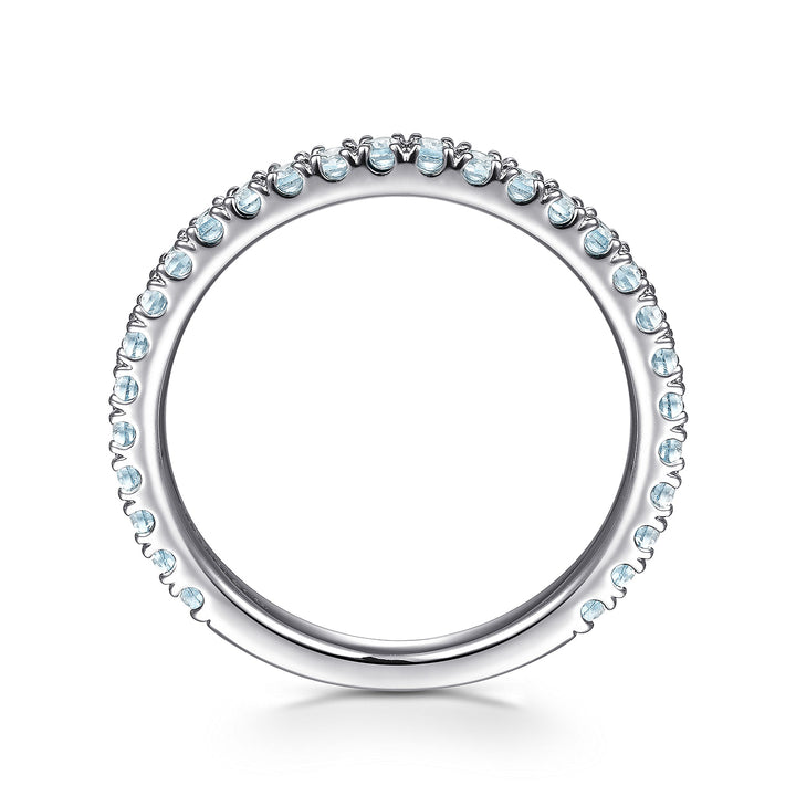 A side profile view of a white gold wedding band against a white background. The ring features sky blue topaz gemstones set in place by small prongs in gleaming white gold.