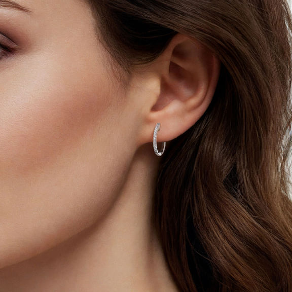 Model wearing Gabriel & Co diamond huggie earrings in white gold, showing how the small hoops sit around the earlobe.