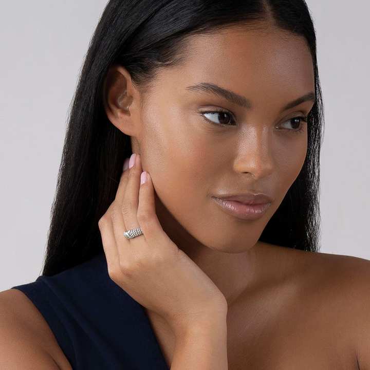 A woman holding her hand up to her cheek, showcasing a sterling silver ring on her ring finger. The ring features an X-shaped design and classic caviar beading.