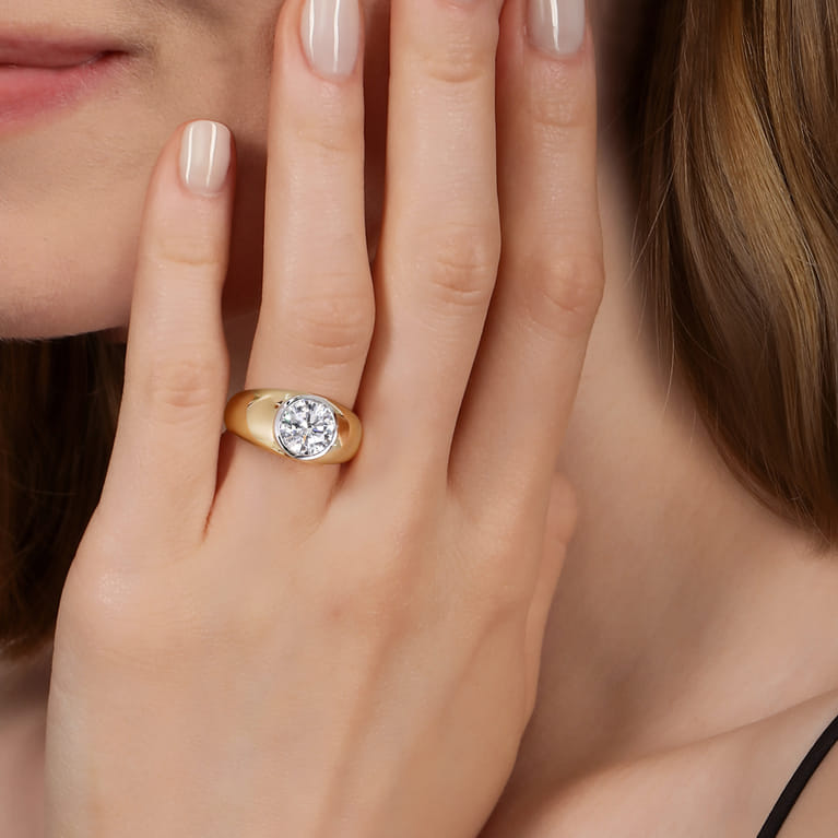 Gabriel & Co. yellow gold dome engagement ring with a bezel-set round diamond worn on a model’s hand.